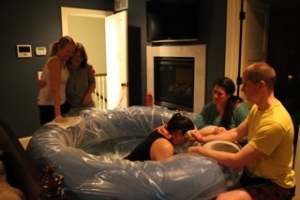 A homebirth mama is comforted by her partner and her doula as her midwives look on. 